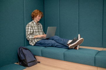 A boy in plaid shirt sitting working on a laptop