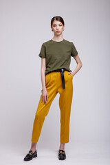 Fashion photo of a beautiful elegant young asian woman in a pretty yellow pants, green t-shirt, belt posing over white, soft gray background. Studio Shot.