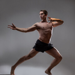 Obraz premium young muscular man in an expressive pose, artistic pose of the hero with outstretched arms. Beautiful muscles. extraordinary athletic body. Portrait on a gray background