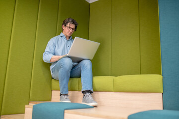 A man in eyewear sitting with a laptop in a lounge zone
