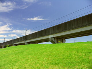 夏の芝生の丘陵とつくばエクスプレス線の高架線と青空