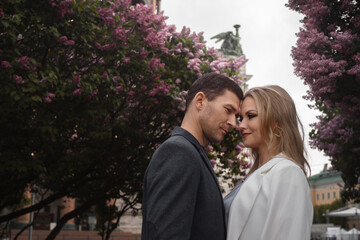 Obraz premium date, a young couple, a man and a woman walking in the city among blooming lilacs