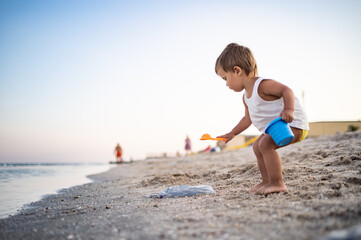 Boy playing with toys on the beach building beads and turrets smiling at someone behind the scenes on summer vacation