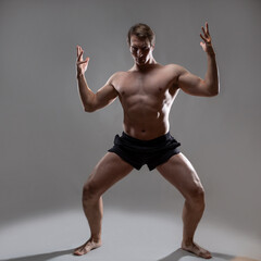 Obraz premium young muscular man in an expressive pose, artistic pose of the hero with outstretched arms. Beautiful muscles. extraordinary athletic body. Portrait on a gray background
