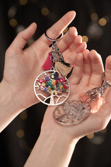 Cropped close-up shot of woman's hands holding two Tree of Life keychains decorated with colored...