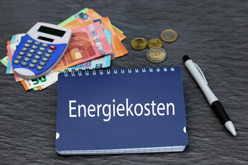 Notiz mit dem Wort Energiekosten  mit Euro Banknoten und Taschenrechner.