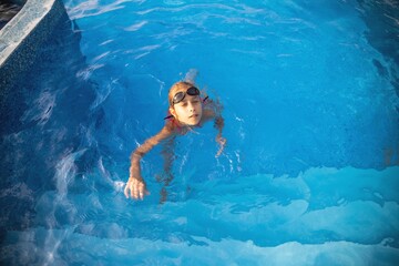A girl in a bright swimsuit with swimming goggles dives into a pool with clear transparent water