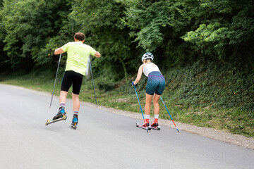 Athletic woman and man together training on the roller ski. Back view. Concept of competition, biathlon, and summer workout