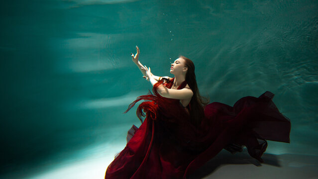 Beautiful Underwater Shooting, A Young Woman In A Red Dress With A Long Skirt Swimming Underwater, Distortion And Caustic Effects.