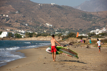 A surfer with his surfboard walking to the beach of Naxos, Greece