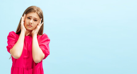 Portrait of beautiful, emotive young girl posing isolated over blue studio background. Sad, tired expression