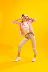 Portrait of young girl posing, cheerfully listening to music in headphones isolated over yellow studio background