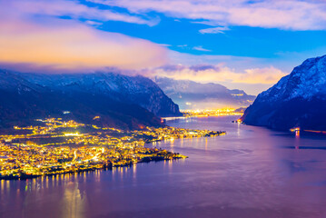 Panorama showing the Lecco shore of Lake Como, on a winter evening, with clouds and snow capped mountains.