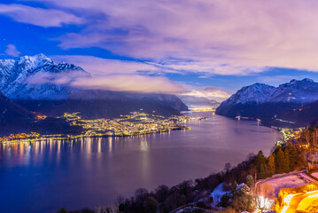 Panorama showing the Lecco shore of Lake Como, on a winter evening, with clouds and snow capped mountains.