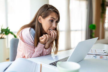 Young woman biting her nails while working on a laptop at home. Anxious woman working in office...