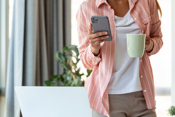 Young business women standing at office and drink coffee looking at smartphone.