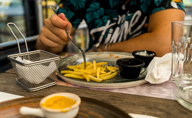 A man is eating fries with ketchup in a restaurant during the day