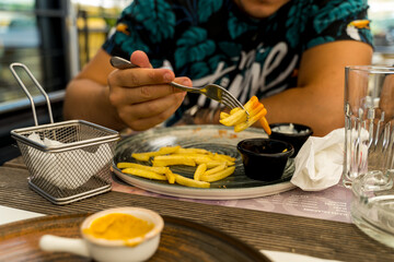 A man is eating fries with ketchup in a restaurant during the day