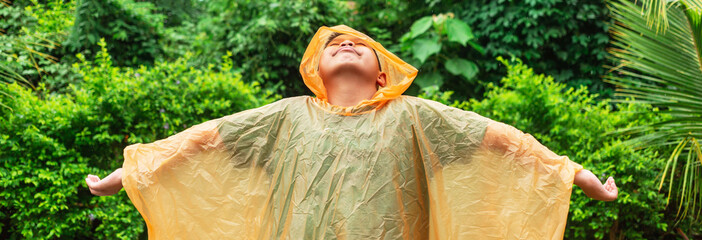 Asian boy wearing orange raincoat is happy and having fun in the rain on a rainy day.