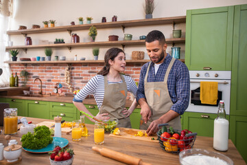 Happy couple multiracial in the morning together at the kitchen preparing the healthy breakfast guy drink a fresh orange juice while his wife cut some vegetables