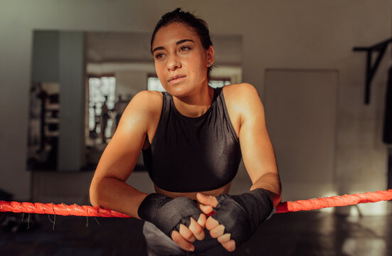 Thoughtful female boxer leaning on boxing ring ropes