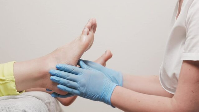 A podologist in blue medical gloves smears cream on a female's foot. Close-up. Slow motion. The concept of chiropody, podology and massage.