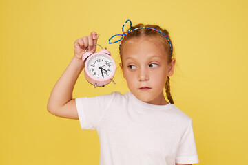 Portrait of a cute girl with a small alarm clock on a yellow background