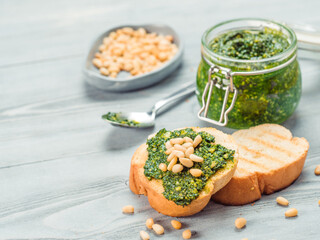 Close up view of baguette bread with fresh basil pesto sauce on gray wooden table. Copy space.