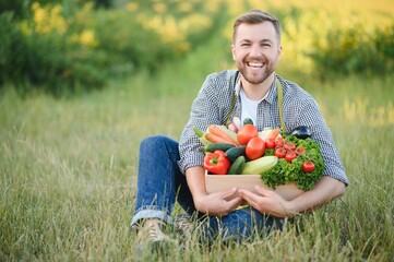 farmer holding a crate of bio vegetables in the farm. Happy man showing box of harvested vegetables.