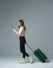 Travel concept. Studio portrait of pretty young woman with suitcase and thinking about something. Isolated on grey.