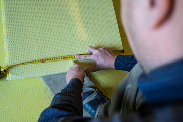The master measures the length of expanded polystyrene on the floor, installation and insulation of...