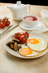 
English breakfast, scrambled eggs with tomatoes and mushrooms, a fabric napkin, a teapot and a cup of tea on the background