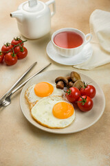 
English breakfast, scrambled eggs with tomatoes and mushrooms, a fabric napkin, a teapot and a cup of tea on the background