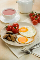 
English breakfast, scrambled eggs with tomatoes and mushrooms, a fabric napkin, a teapot and a cup of tea on the background