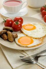 
English breakfast, scrambled eggs with tomatoes and mushrooms, a fabric napkin, a teapot and a cup of tea on the background