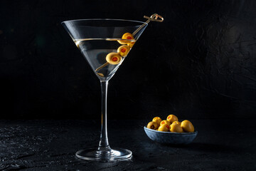Martini, a glass with spicy olives on a toothpick, on a black background. Alcoholic cocktail