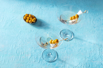 Martini, two glasses with spicy olives on toothpicks, on a blue background. Alcoholic cocktail