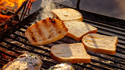 Pieces of white bread are grilling on the open fire outside,