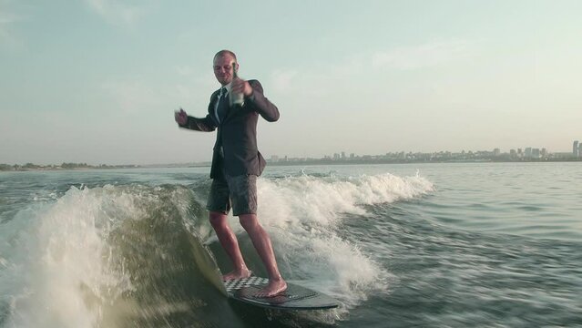 A happy surfer jumping on a wakeboard in a suit with a bottle of champagne. An experienced wakeboarder sprays water drops into the camera.