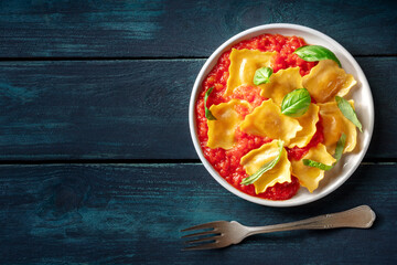 Ravioli with tomato sauce and fresh basil, Italian dumplings, top shot on a wooden table with a fork and a place for text