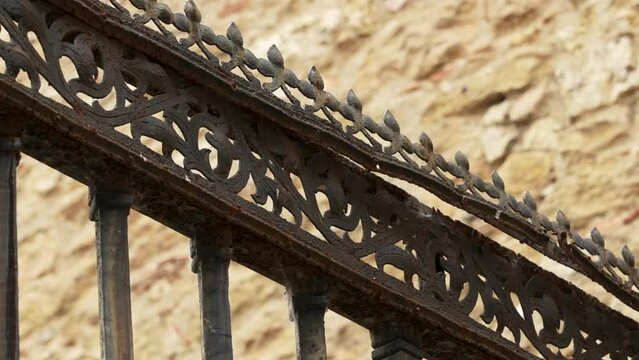 Black patterned forged iron fence with spikes and peaks of an antique medieval cathedral with a weathered stone wall in blur. Security concept