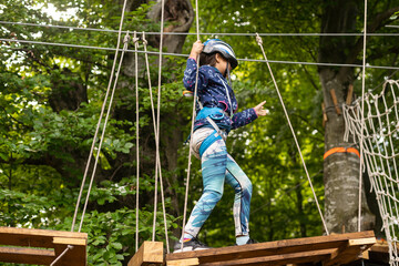 Little girl preschooler wearing full climbing harness having fun time in the rope park using carabiner and other safety equipment. Summer camp activity for kids. Adventure park in the forest