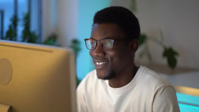 Closeup of pleased young black man web designer or graphics editor enjoying remote work at cozy and comfortable home office space, joyful African guy it-specialist working remotely on desktop computer