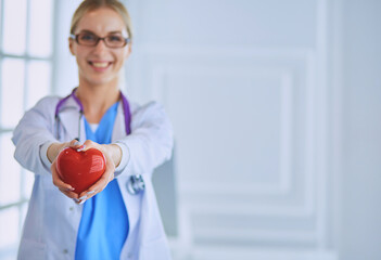 Female doctor with stethoscope holding heart in her arms. Healthcare and cardiology concept in...