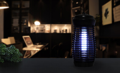 an insects mosquito electric blue light killer lamp is put on the black wooden table in the dark office working room to protect the mosquito during working time