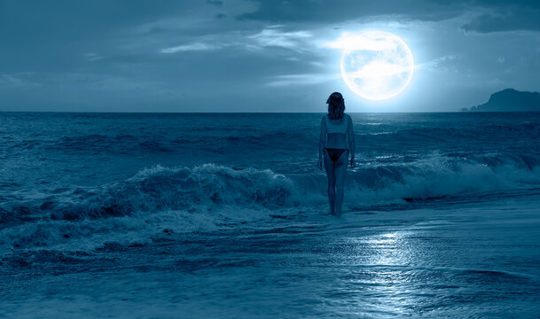 Silhouette of a beautiful girl standing on the beach, full moon in the background "Elements of this image furnished by NASA 