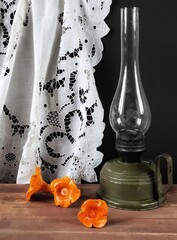 Rustic still life with retro kerosene lamp on a wooden table, handmade clay chanterelle, white curtain and copy space. 