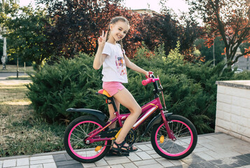 Girl child is dressed in summer clothes and rides a bicycle. Happy smiling child sits on a bike and...