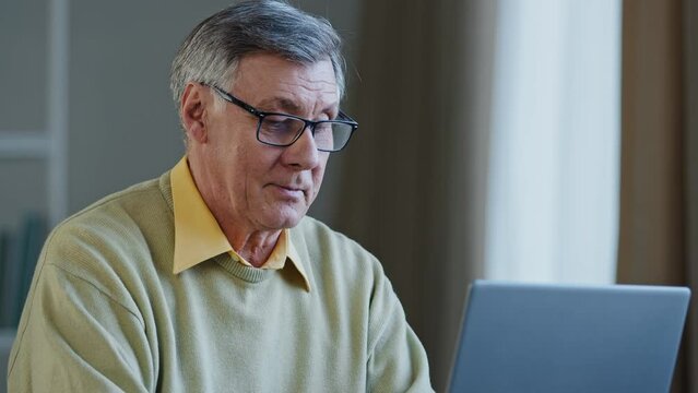 Close-up serious pensive old male writer journalist author businessman grandpa thinks about idea searching solution problem in thought enthusiastic typing on laptop showing thumb up celebrate success