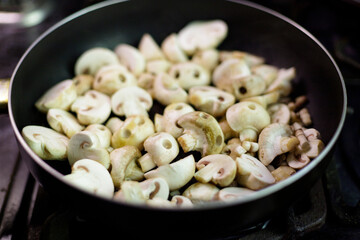 Mushrooms in the form of skulls in black frying pan. Champignons frying process. Edible Halloween Concept